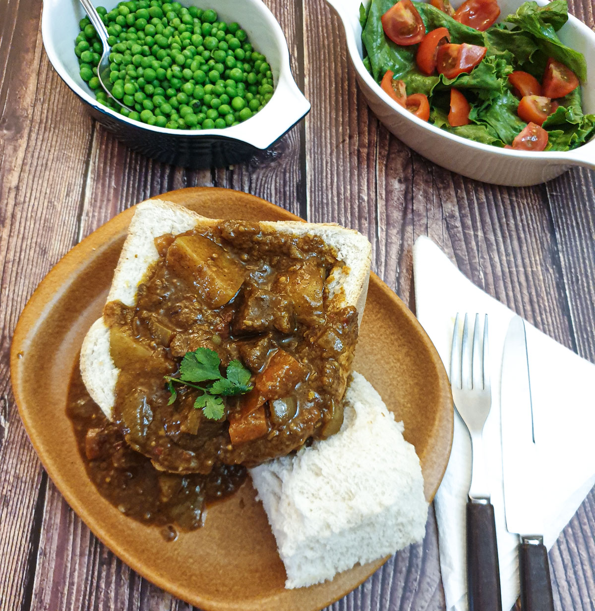 A bunny chow on a brown pate with bowls of side dishes in the background.