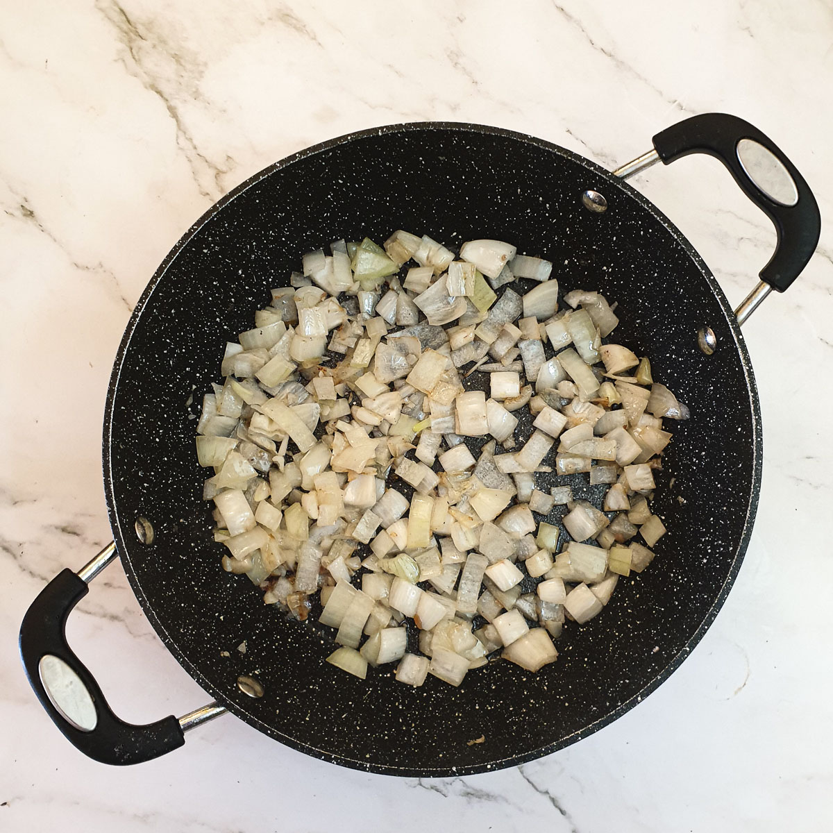 Chopped onions being cooked in a frying pan.