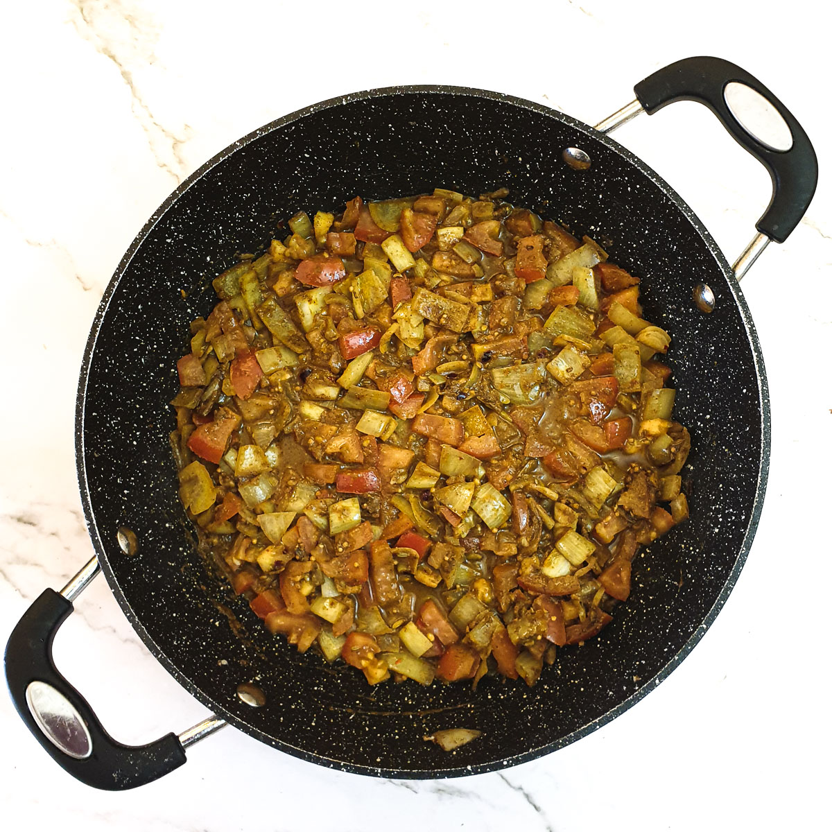 Tomatoes frying with onions and spices in a frying pan.