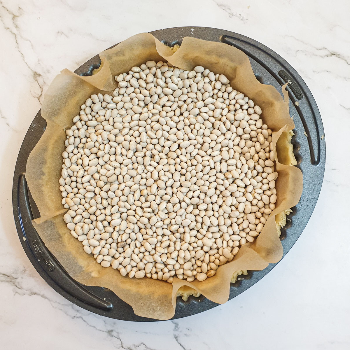 A pastry case lined with baking parchment and filled with dry beans.