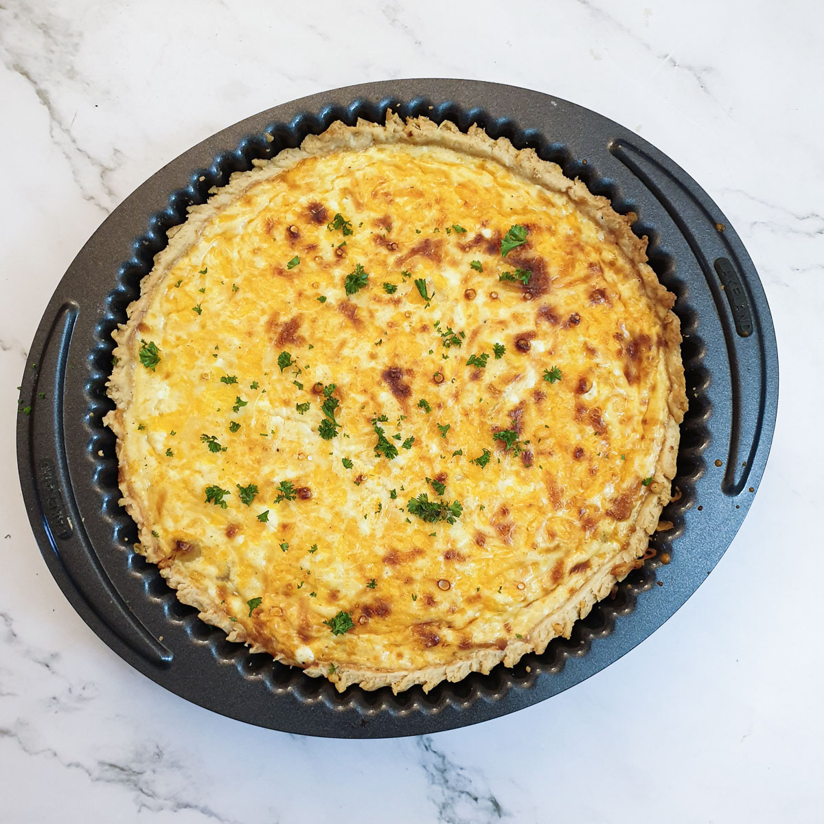 A baked cheese and onion quiche sprinkled with chopped parsley.