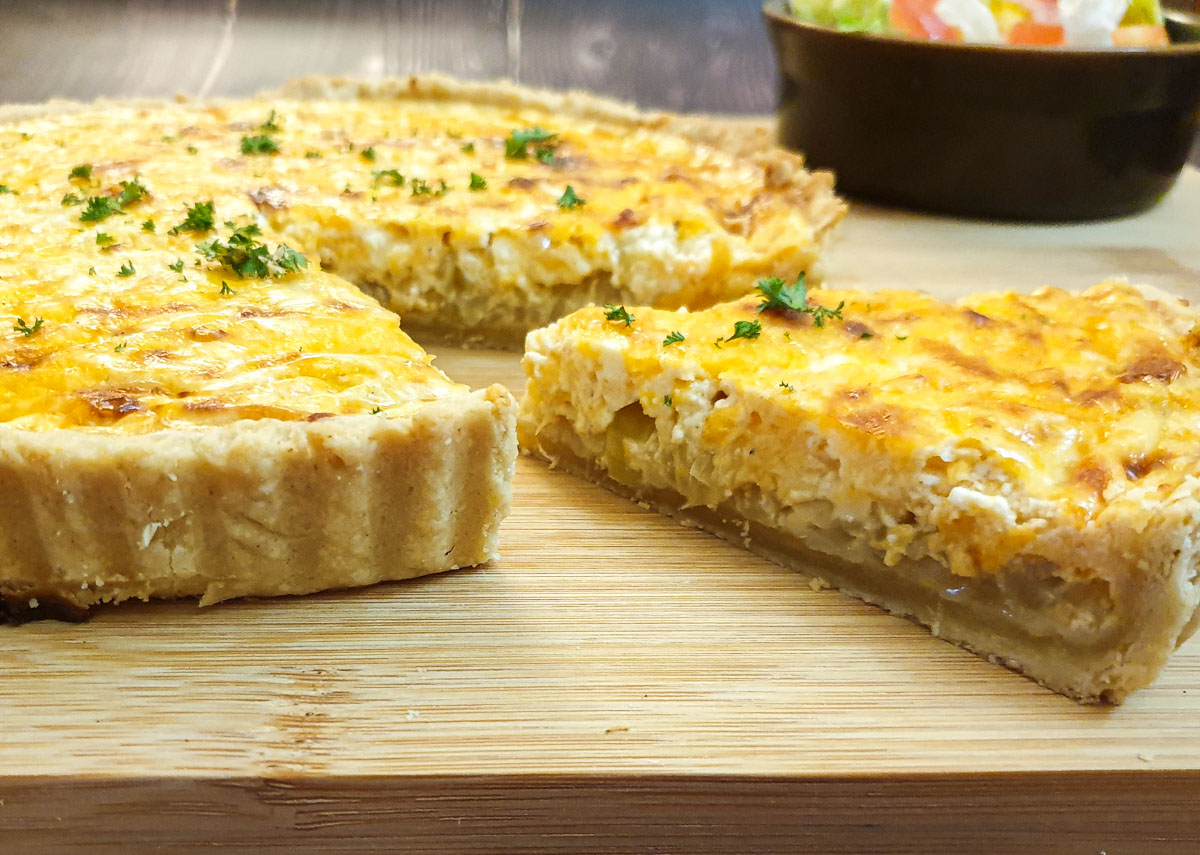 Closeup of a slice of cheese and onion quiche on a wooden board.