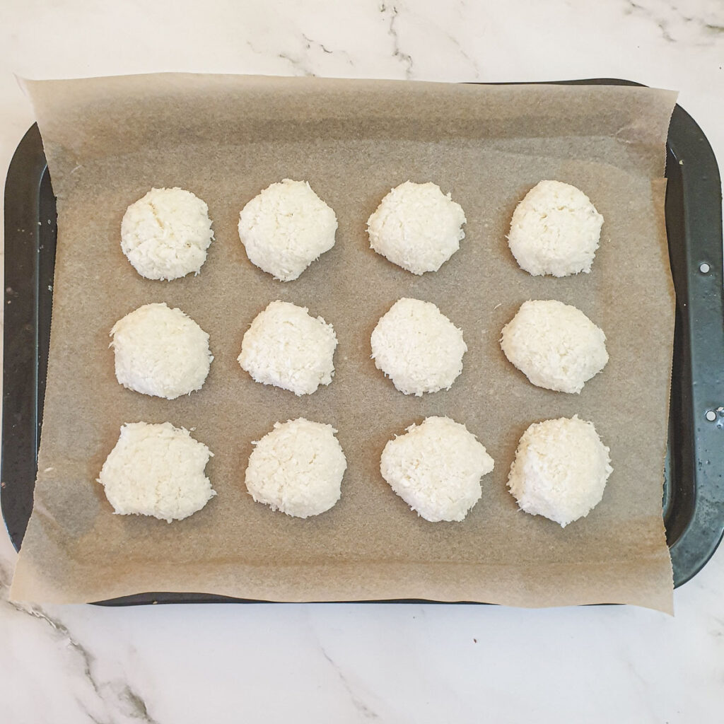 12 unbaked coconut macaroons on a baking tray.