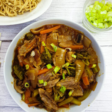 A dish of duck in garlic sauce with vegetables next to a dish of pasta.