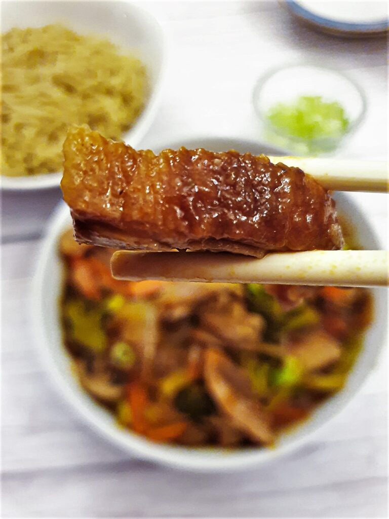 A piece of crispy duck held in chopsticks.