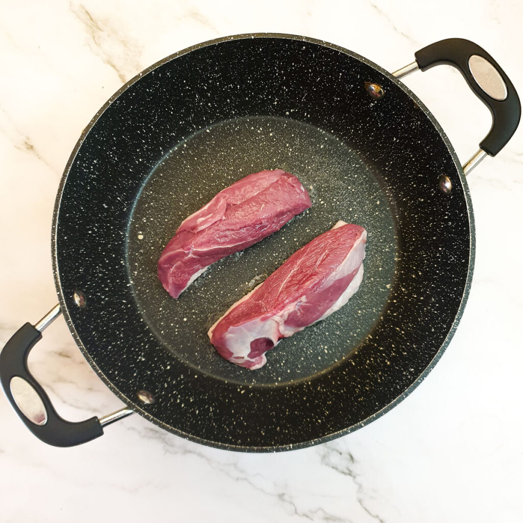 Two duck breasts skin side down in a frying pan.