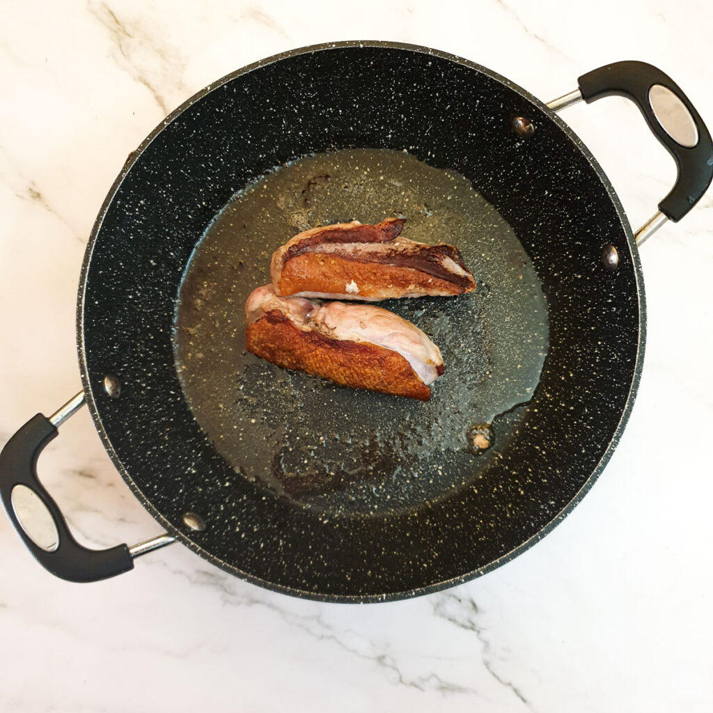 Two duck breasts in a frying pan showing the crisped skin.