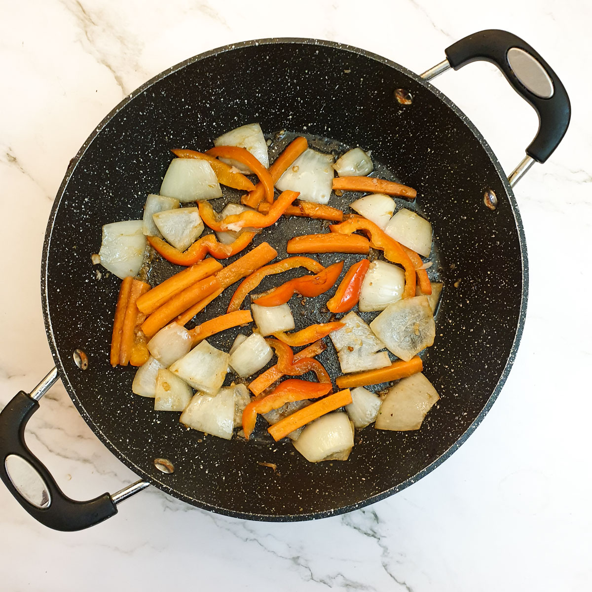 Sliced onions, carrots and red peppers in a frying pan.