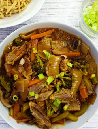 A dish of duck in garlic sauce with vegetables next to a dish of pasta.