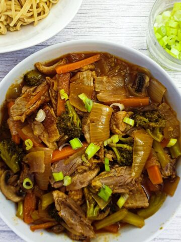 A dish of duck in garlic sauce with vegetables next to a dish of pasta.