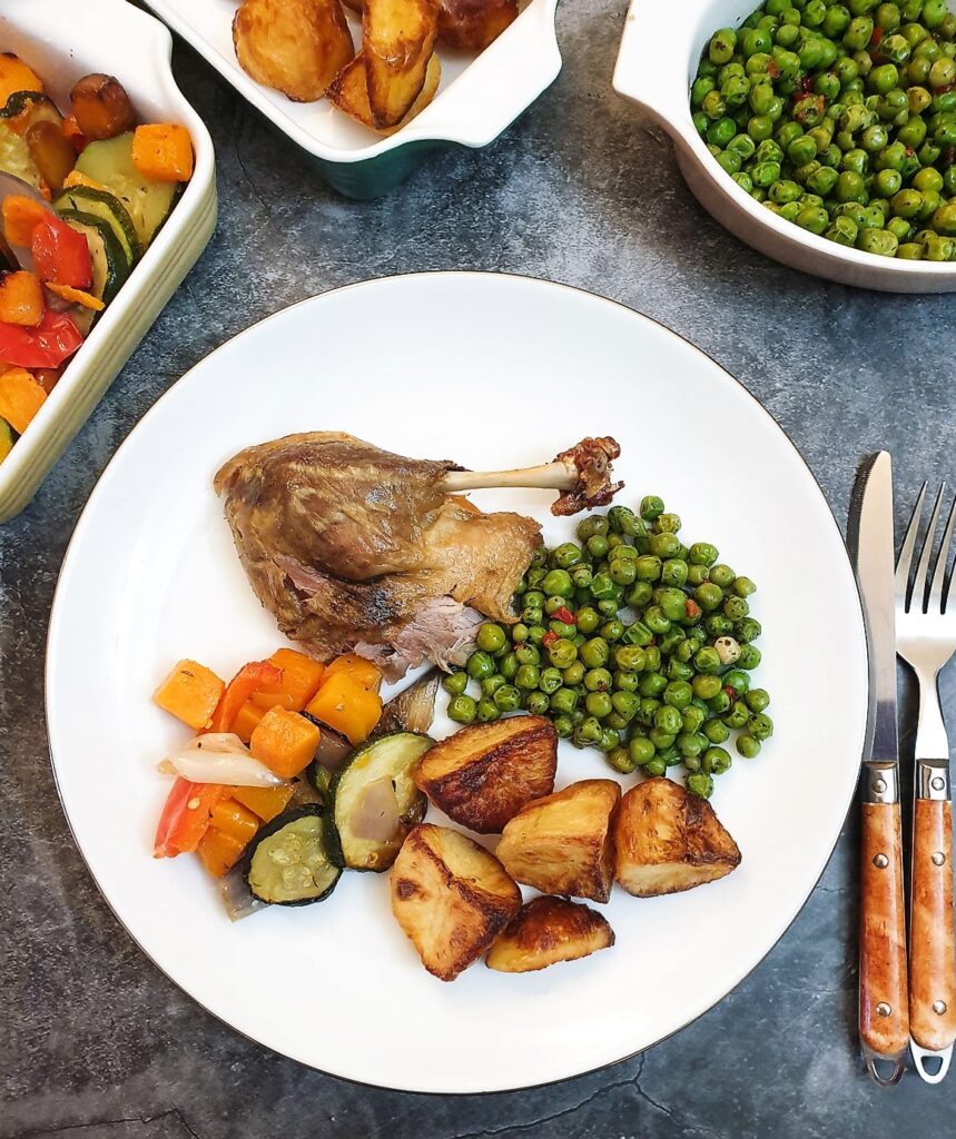 A crispy duck leg on a plate with vegetables.