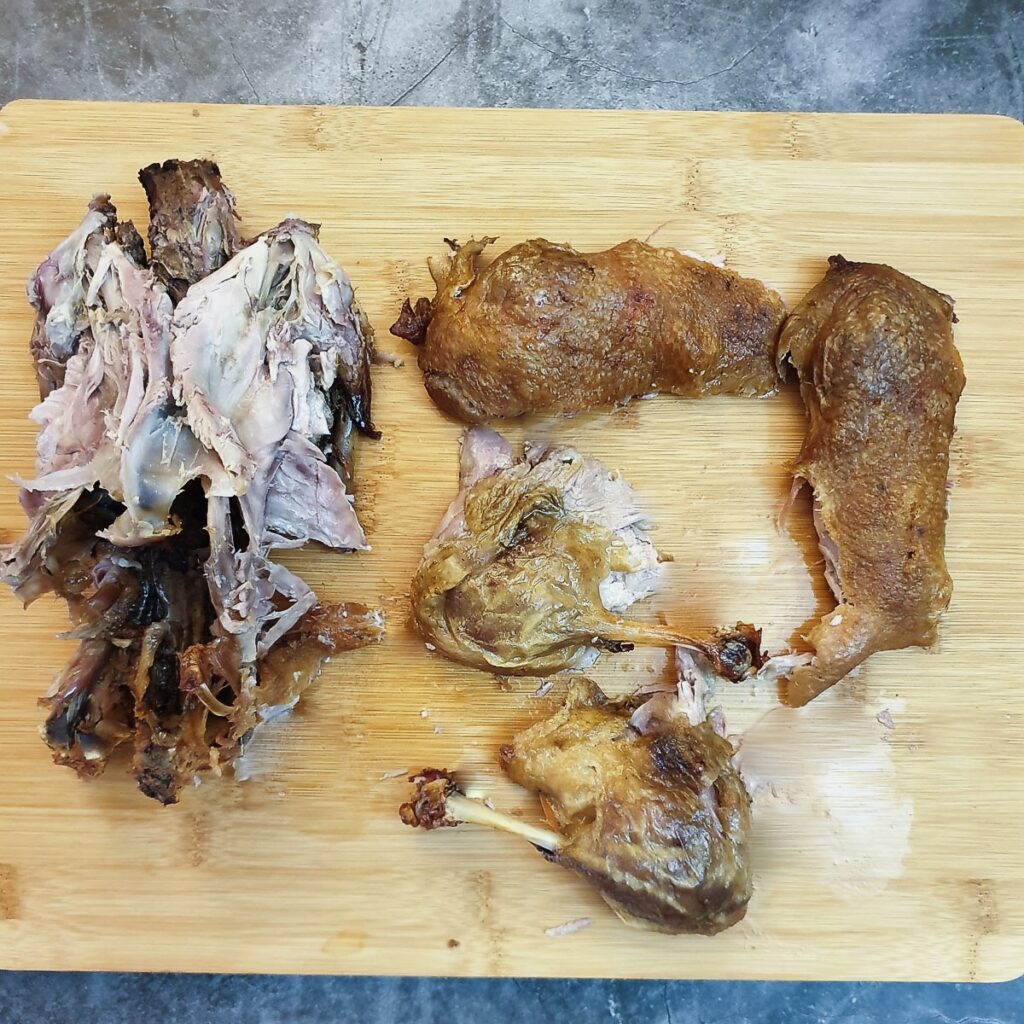 A roast duck carcass next to the legs and breasts that have been removed.