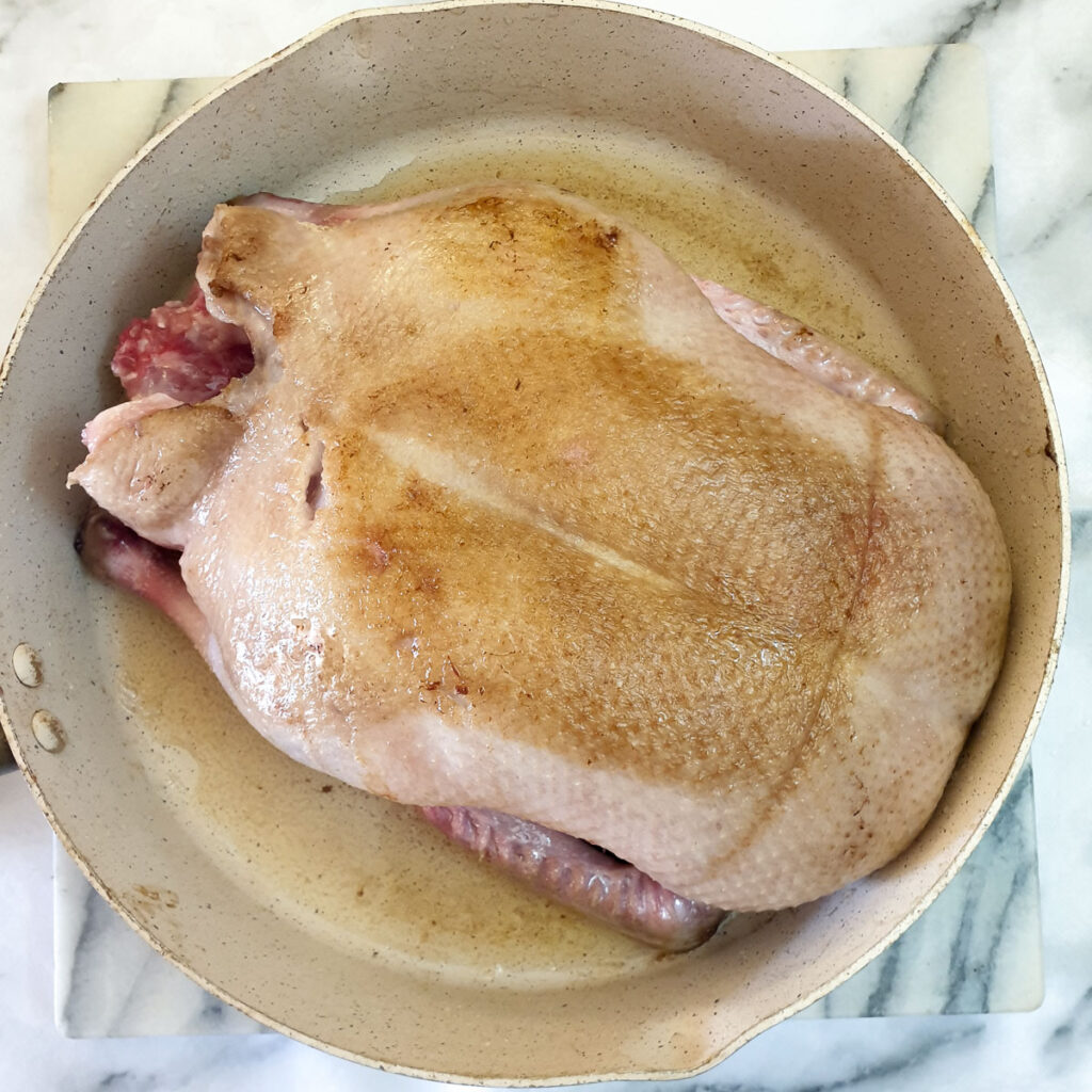 A whole duck being browned in a frying pan.