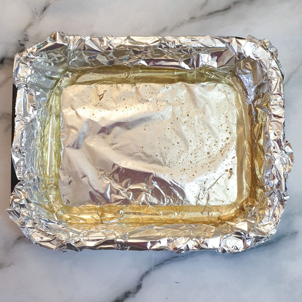 A roasting tray lined with tinfoil containing duck fat.