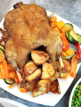 A roast duck on a serving plate with roast potatoes and vegetables.