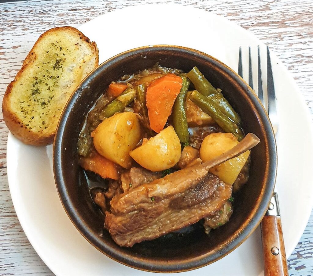 Lamb bredie in  dish with a slice of crusty bread.