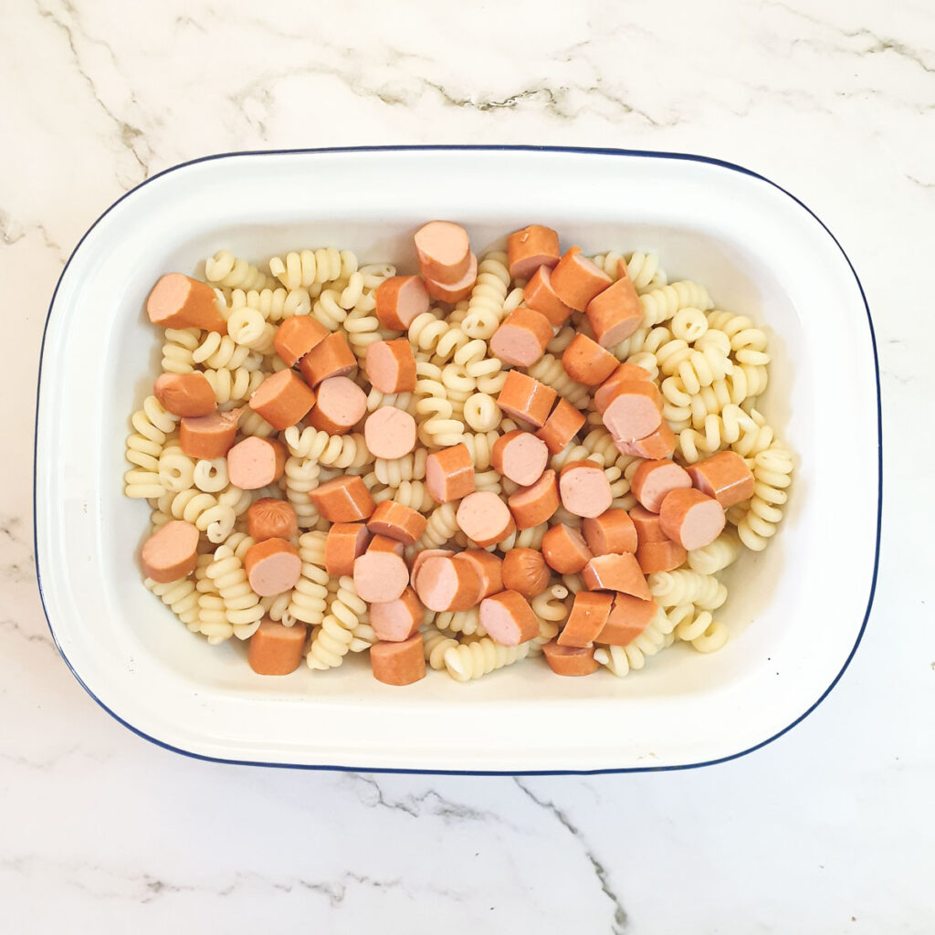 Pasta and chopped sausages in a baking dish.