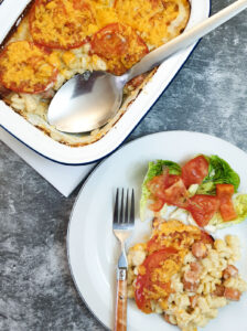 A serving dish of macaroni cheese next to a helping on a plate.