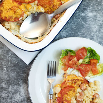 A serving dish of macaroni cheese next to a helping on a plate.