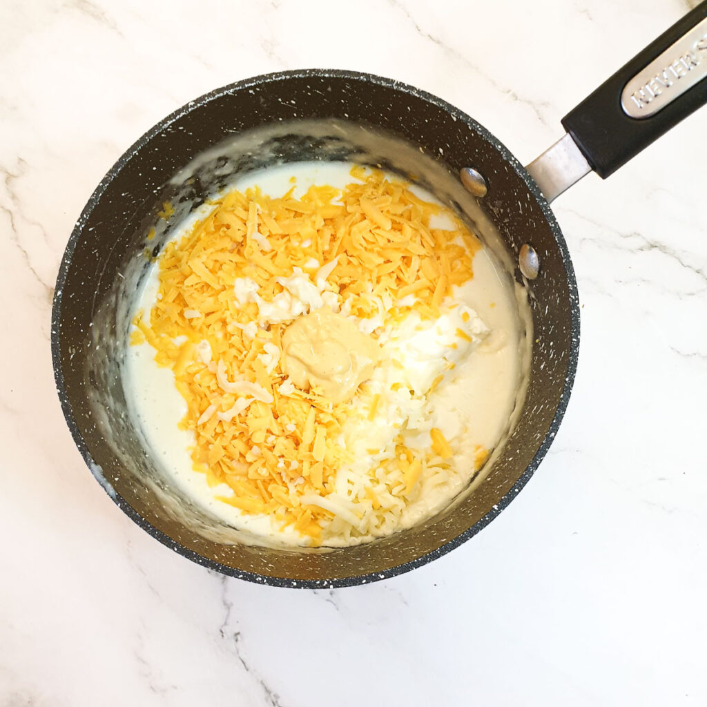 Grated cheese being added to the sauce in a saucepan.