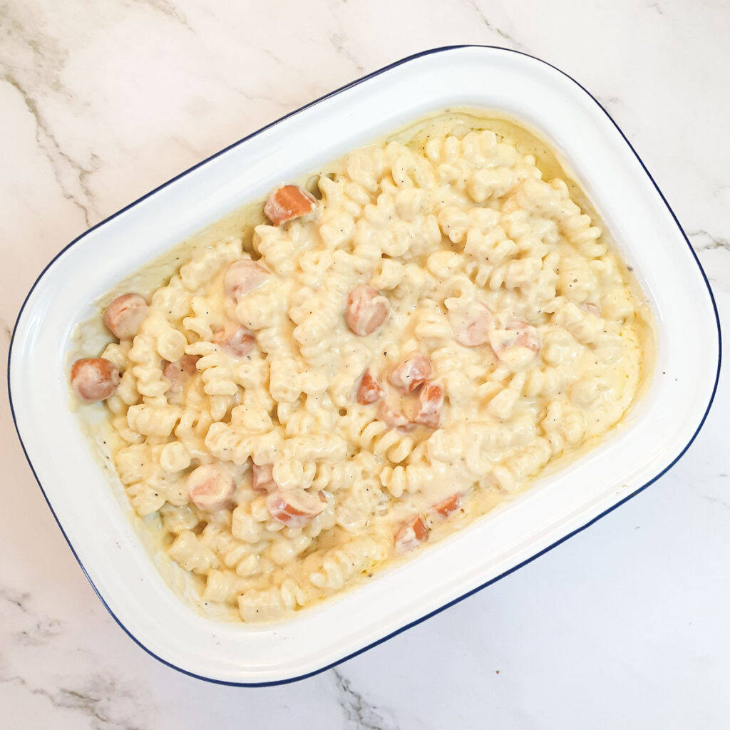 Pasta and sausages in a baking dish mixed with cheese sauce.