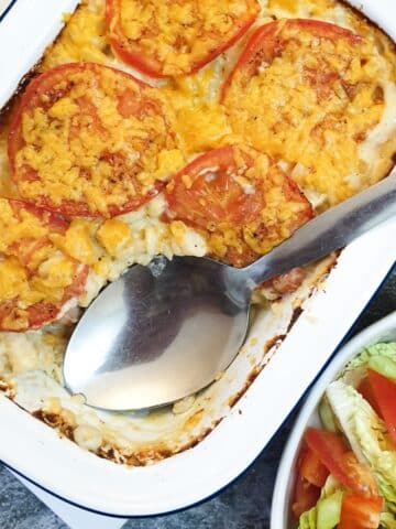 A white dish of macaroni cheese with a large serving spoon.