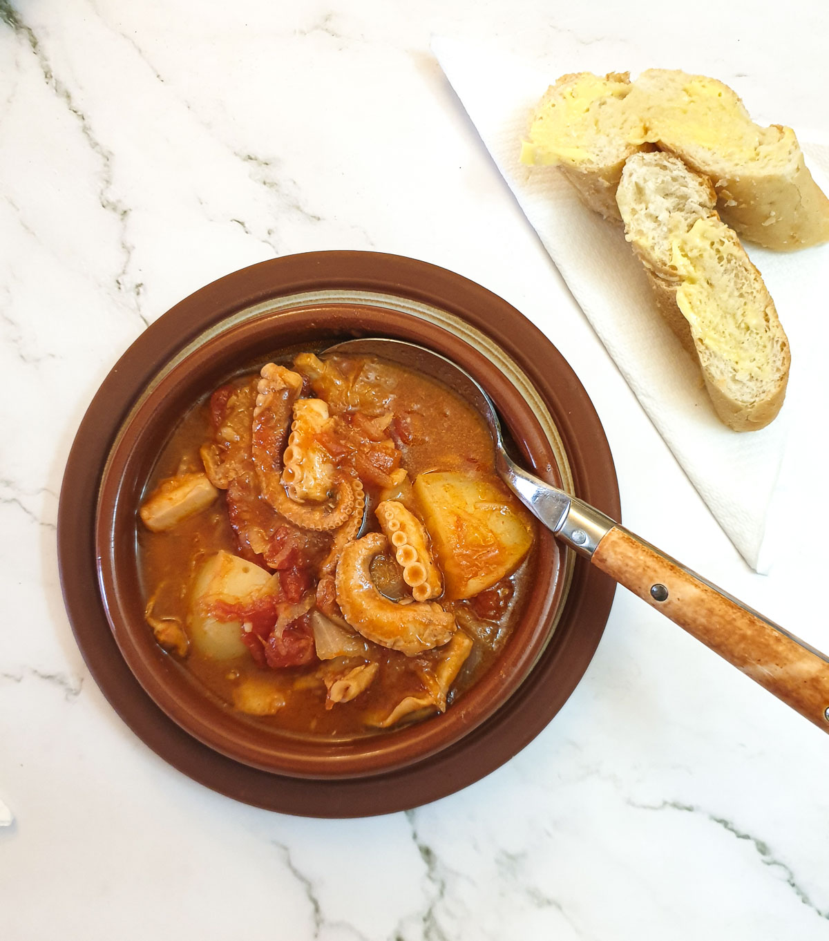 Overhead stot of octopus stew with 2 slices of crusty bread on a napkin.