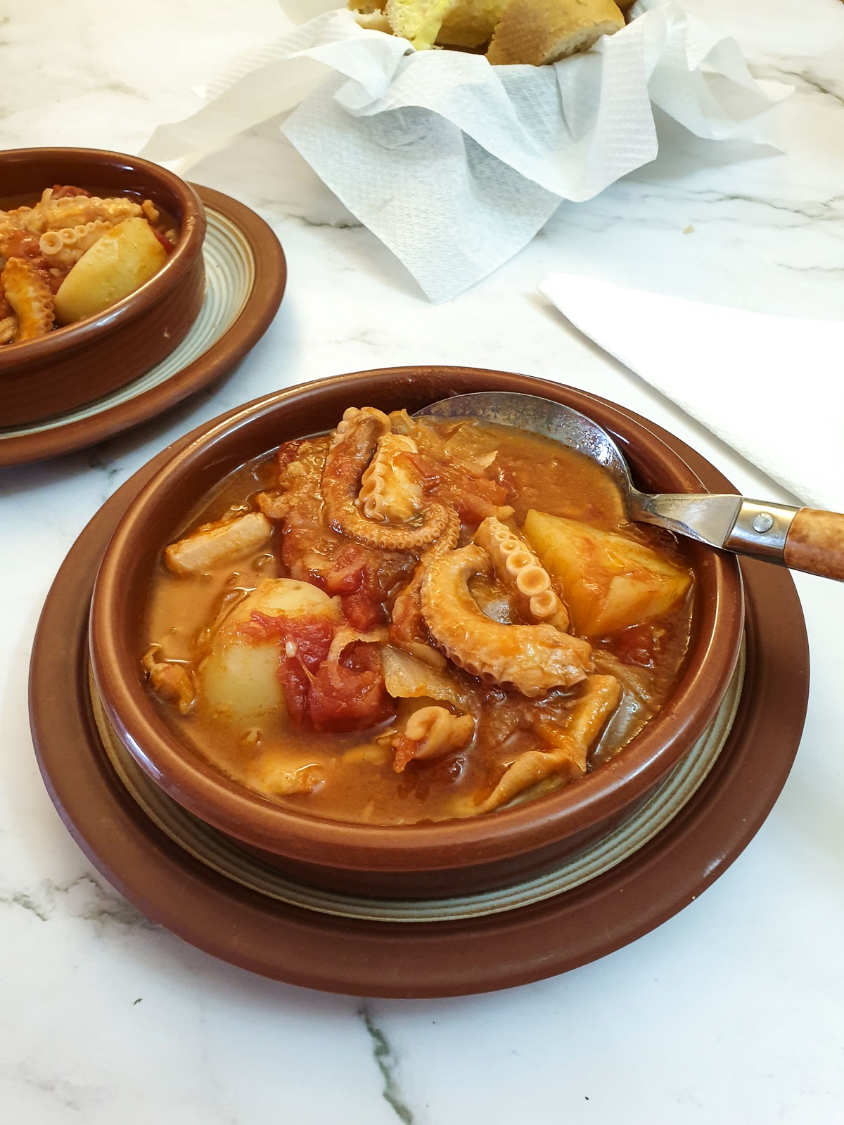 Octopus stew in tapas dishes next to a bowl of crusty bread.