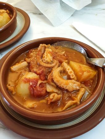 Octopus stew in tapas dishes next to a bowl of crusty bread.