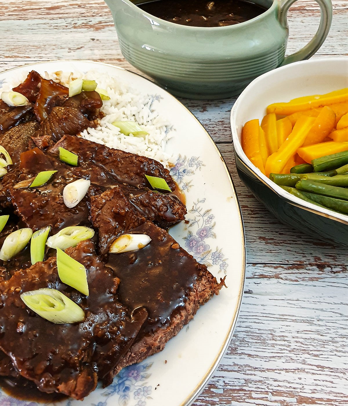 Slices of mongolian beef on a serving plate next to a bowl of vegetables.