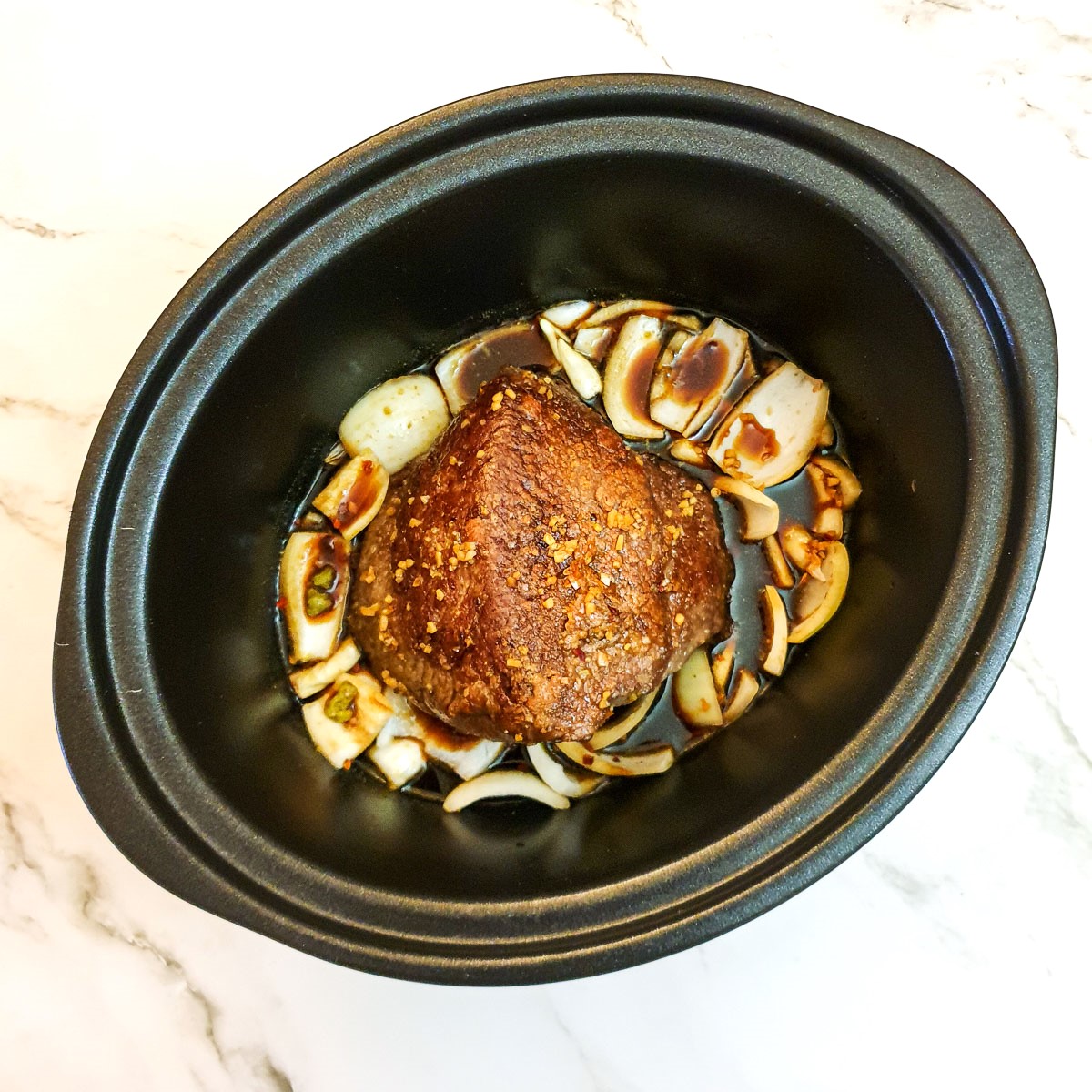 Onions and a beef joint in a slow cooker, covered with stock.