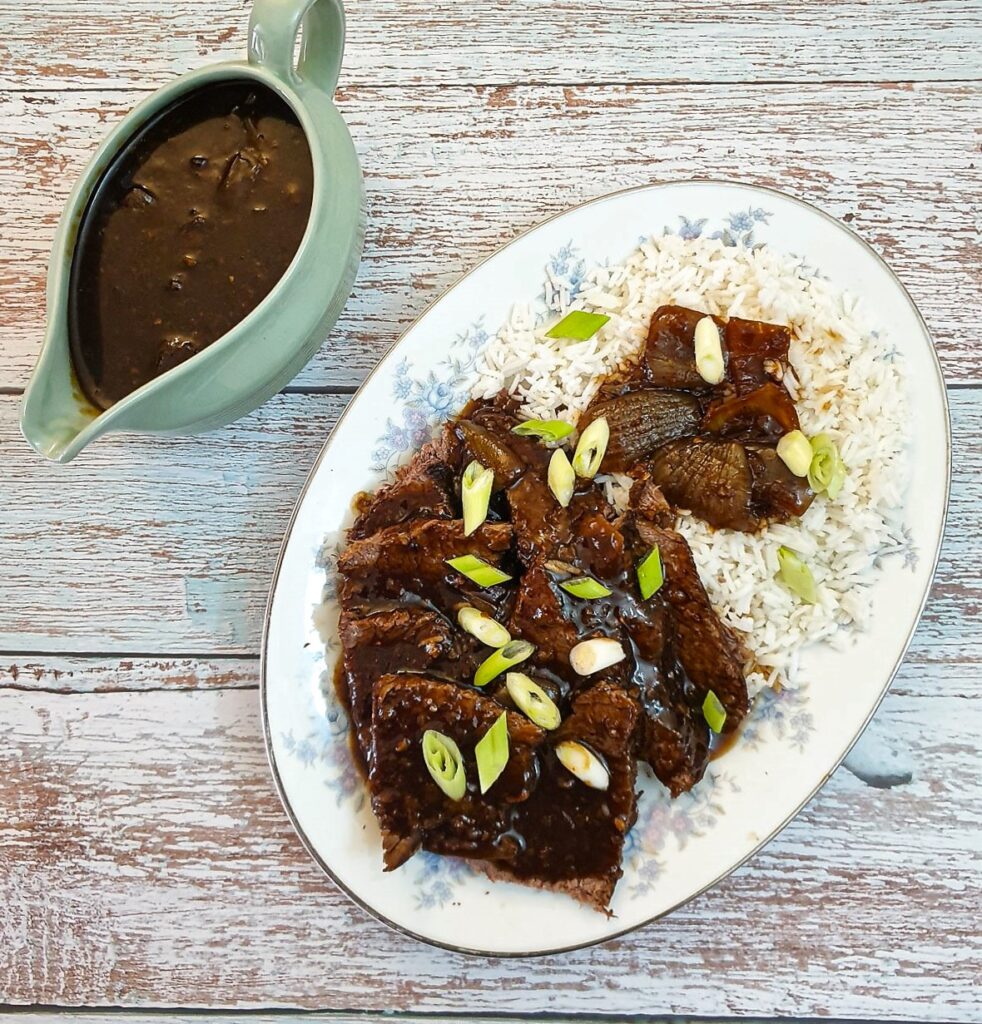 Slices of slow-cooker mongolian roast beef on a bed of rice.