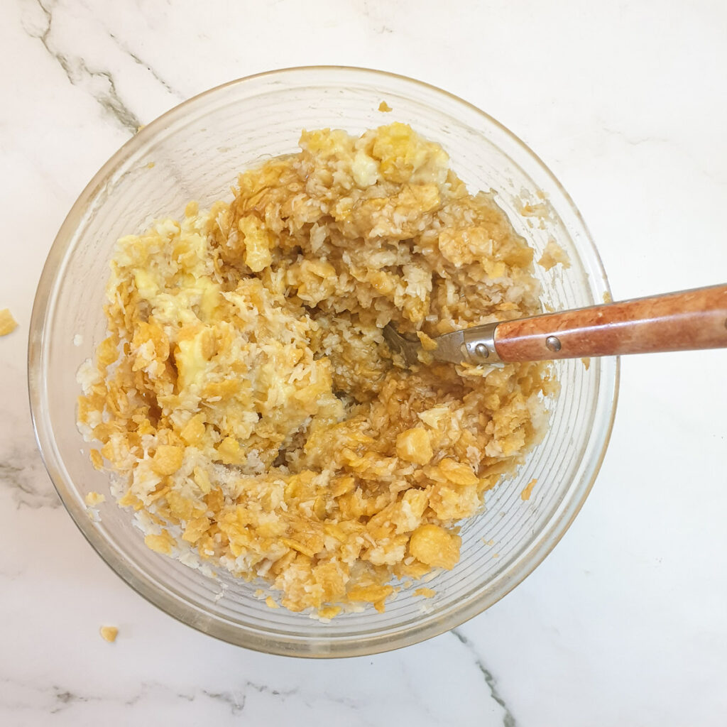 Cornflakes, honey and melted butter being added to the bananas and coconut.