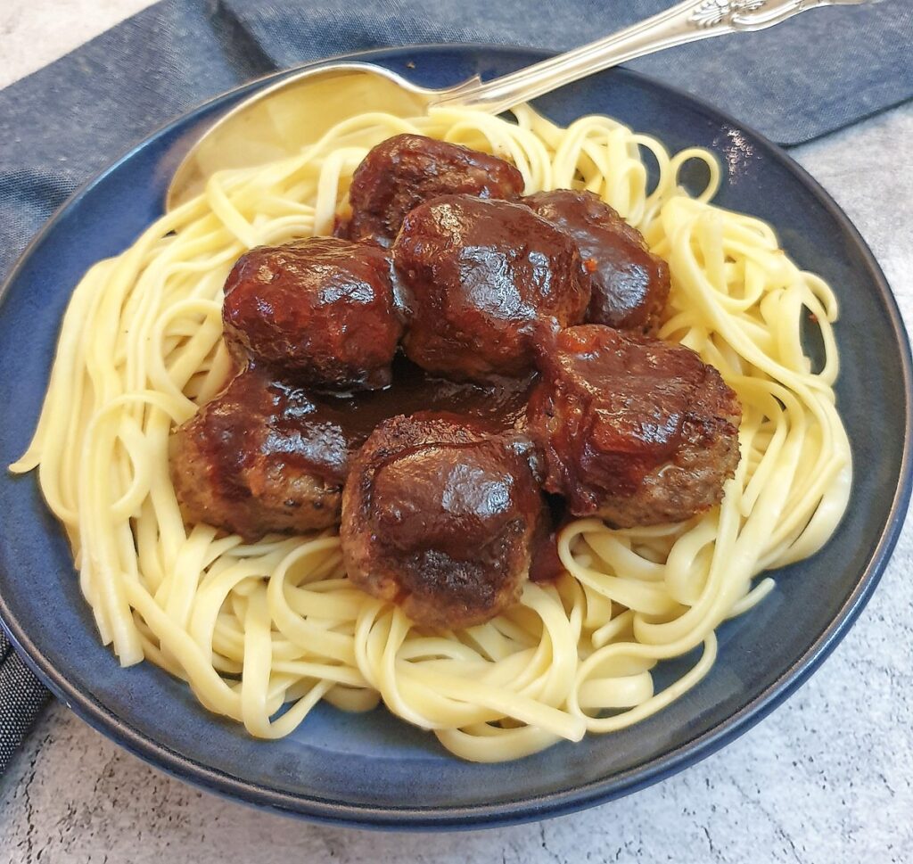 Meatballs on a bed of linguine covered with barbeque sauce.