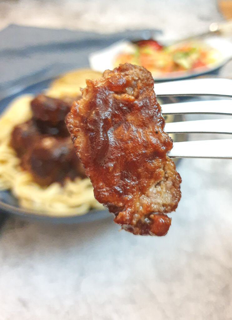 Half a meatball on a fork, covered in barbeque sauce.