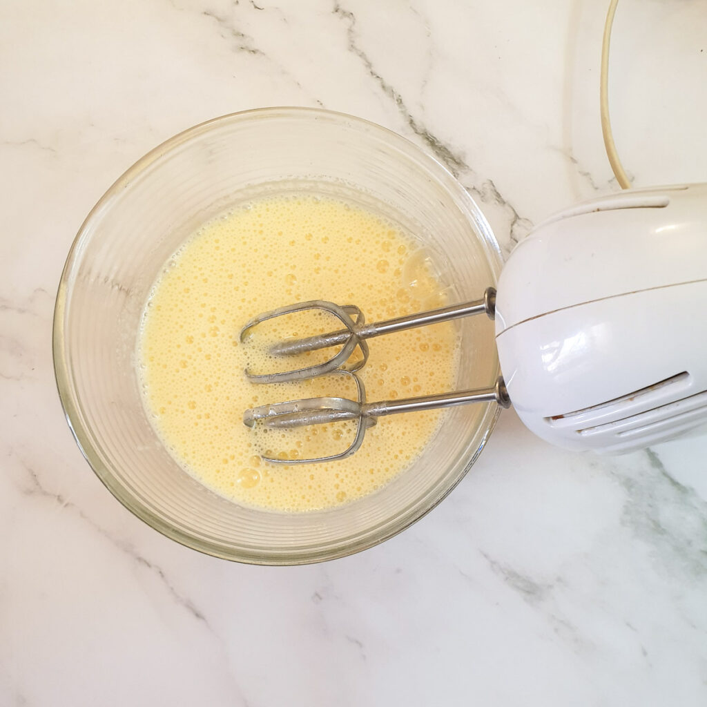 A bowl of eggs nd sugar being whipped in a glass bowl.