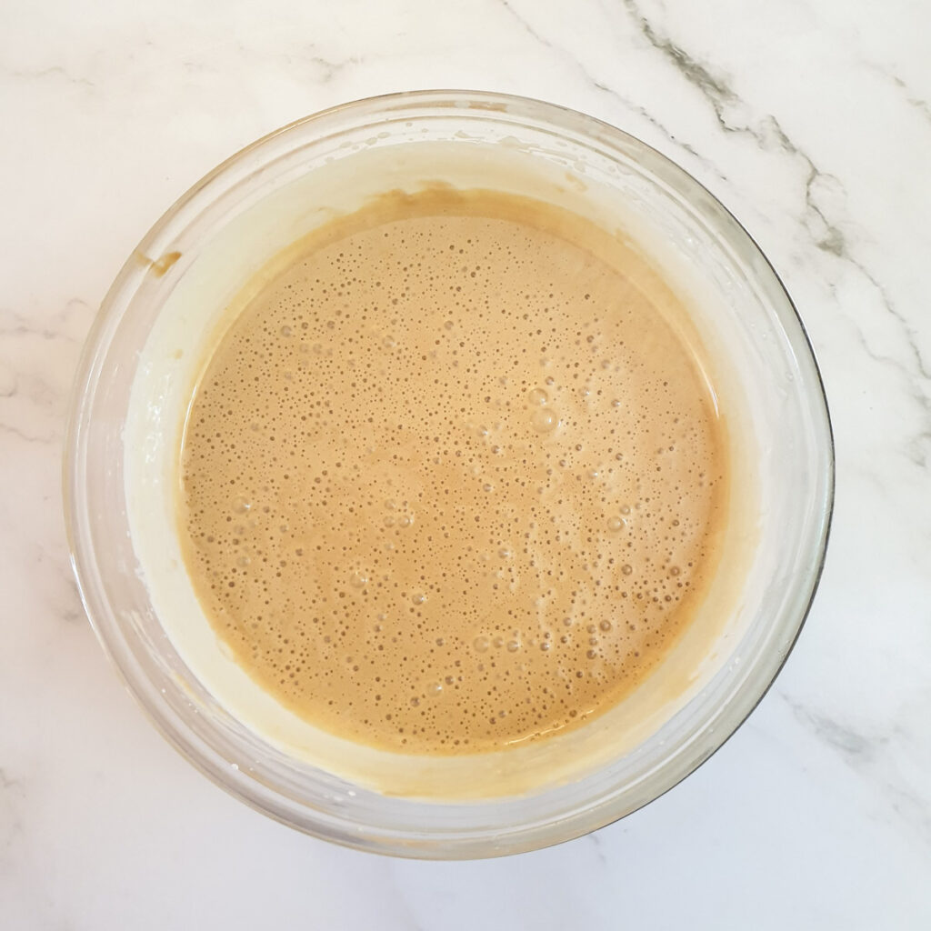 A glass bowl containing a mixture of eggs, sugar and Biscoff spread.