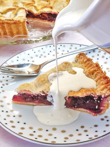 A jug of cream being poured over a slice of blackberry and apple pie.