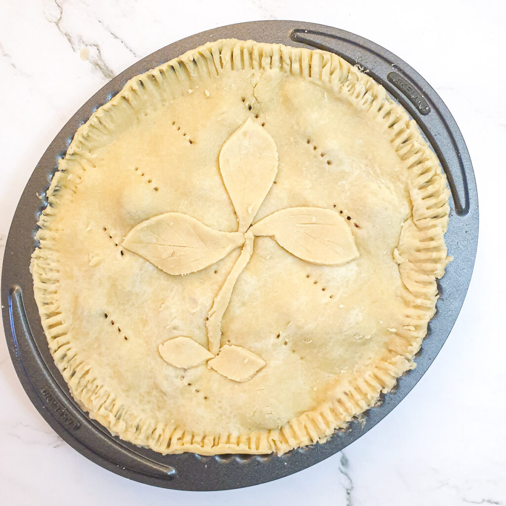 An unbaked pie in a baking dish decorated with pastry leaves.