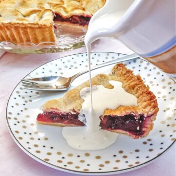 A jug of cream being poured over a slice of blackberry and apple pie.