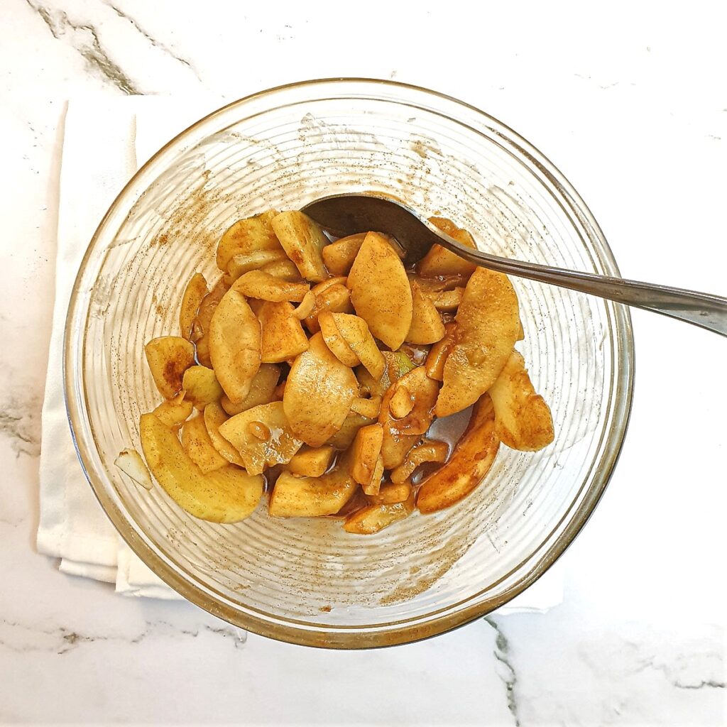 Sliced apples in a mixing bowl atter being mixed with sugar.