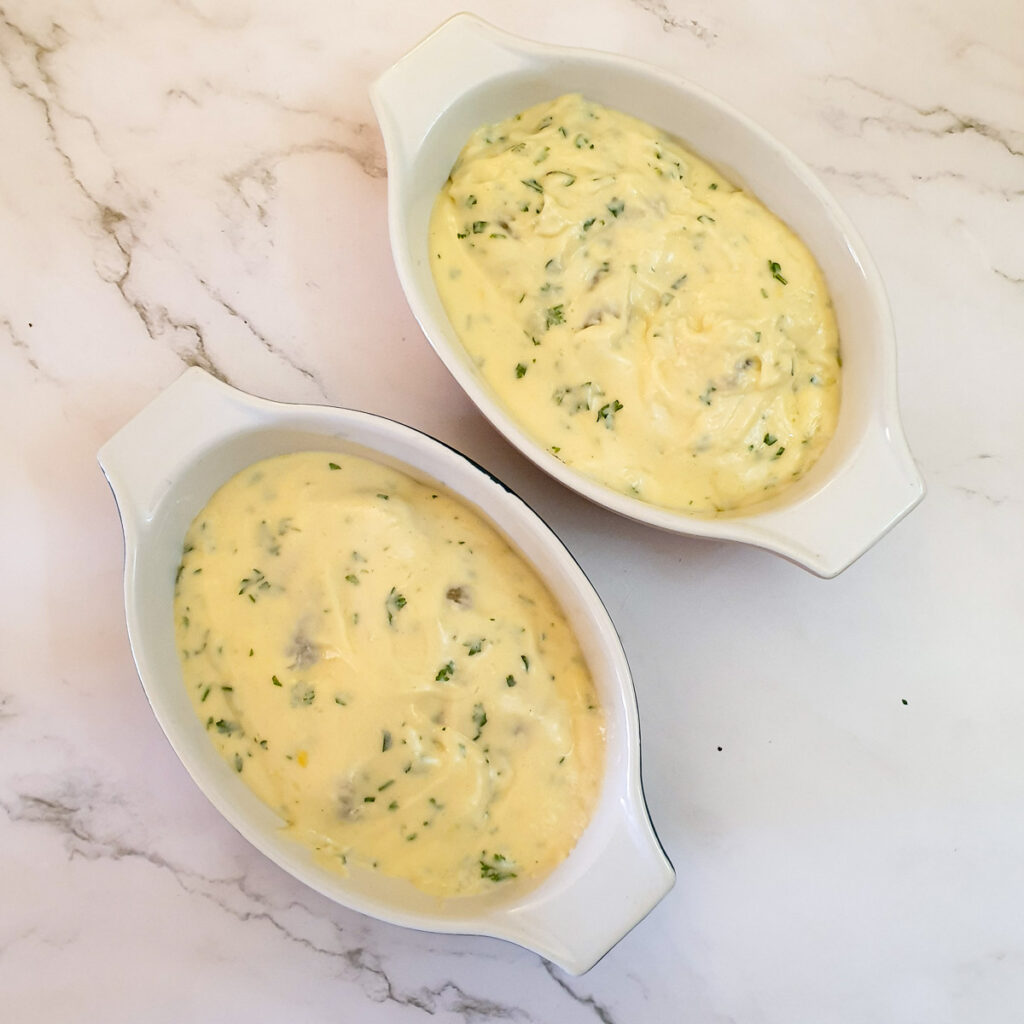 Cheese sauce covering the fish and prawns in 2 small serving dishes.