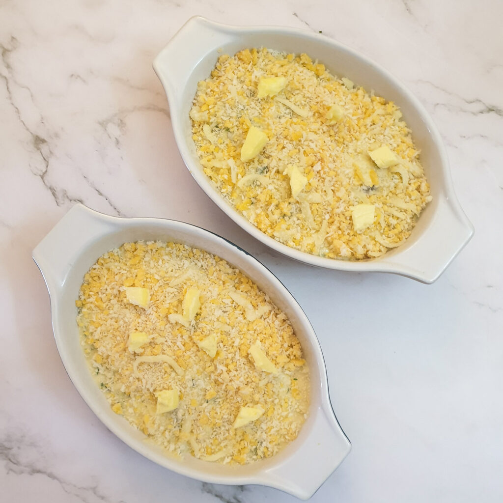 Two dishes containing cod mornay topped with breadcrumbs and butter.