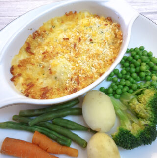 Cod mornay in an individul serving dish on a plate with steamed vegetables.