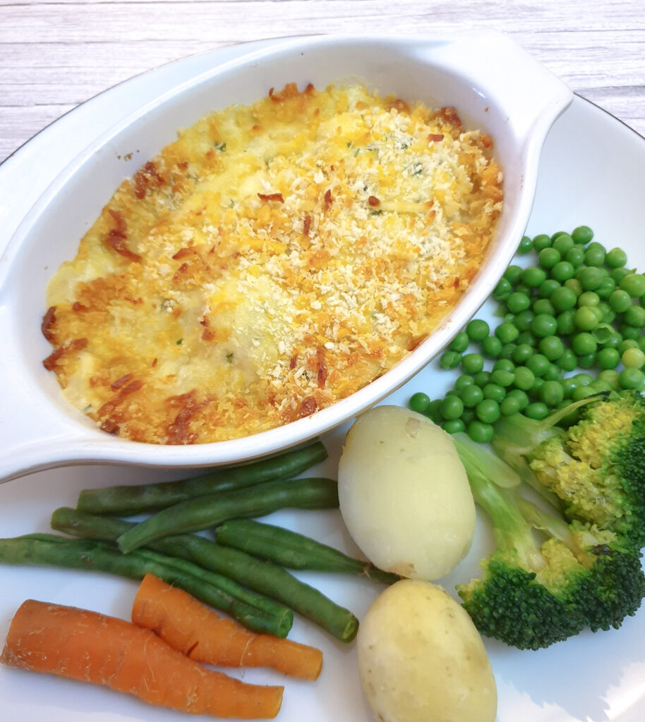 Cod mornay in an individul serving dish on a plate with steamed vegetables.