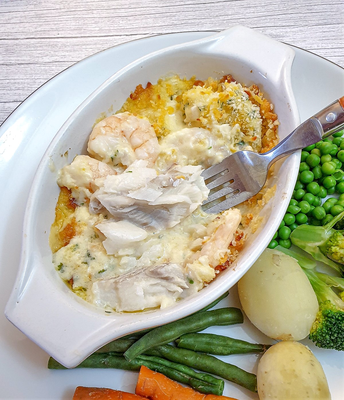 Close up of cod mornay, showing the flaky fish and prawns under the cheese sauce.