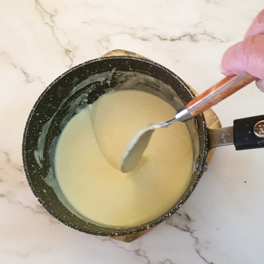 A spoon drawing a trail through a pan of bechamel sauce.