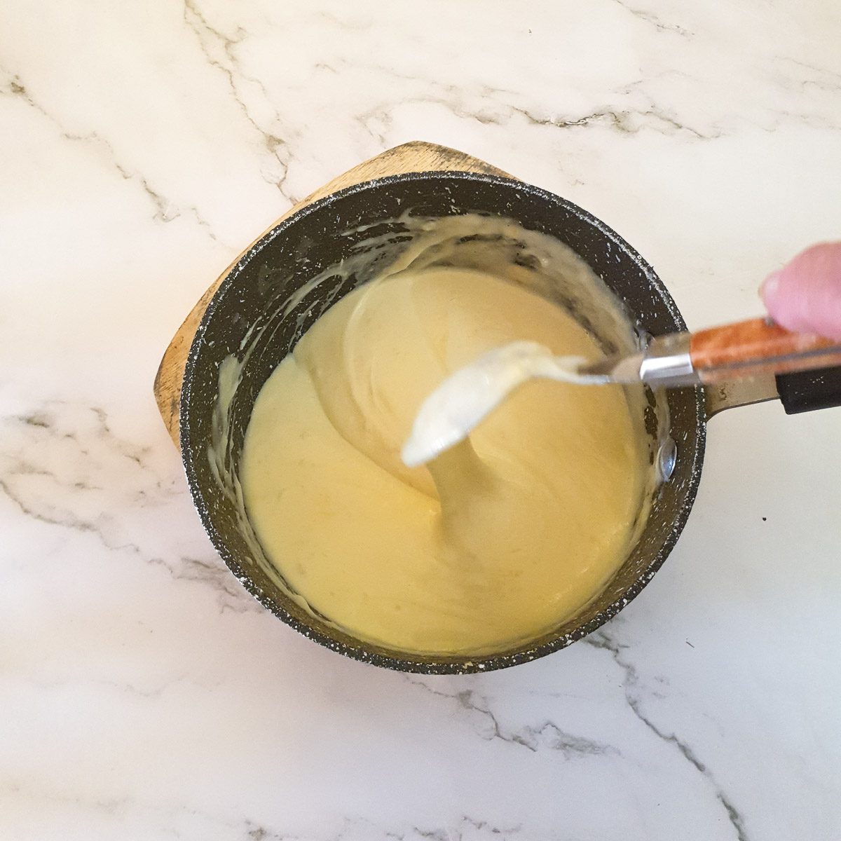 A spoon drawing a trail through a pan of cheese sauce.