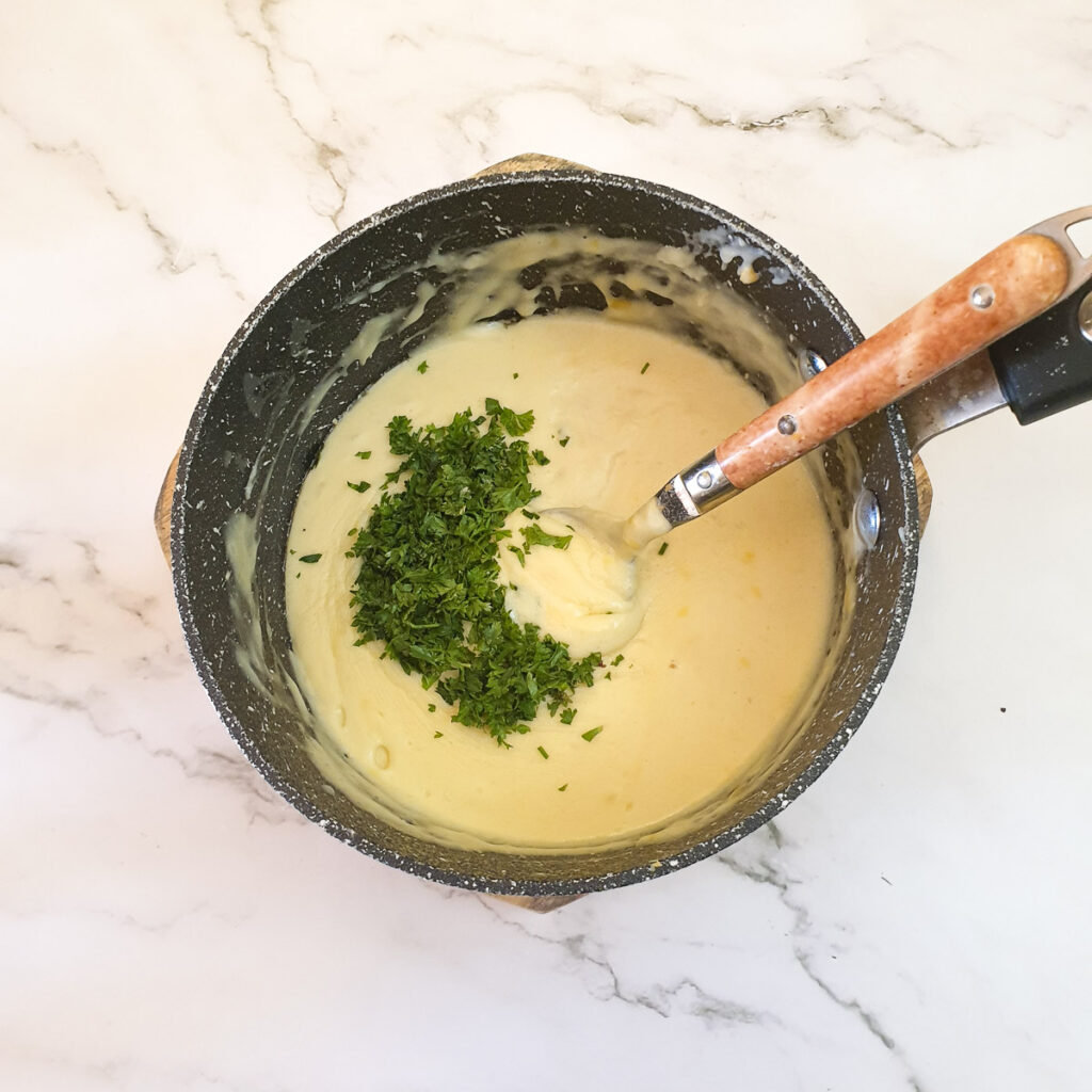 Chopped parsley being added to a pan of mornay sauce.