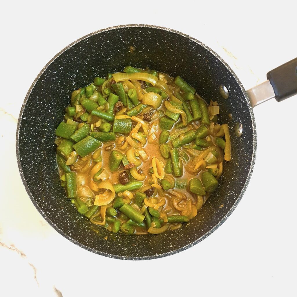 Green beans in saucepan with onions and sauce ingredients.